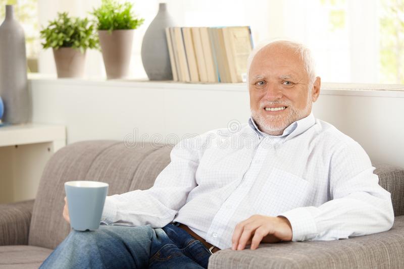 Smiling Elderly Man Having Coffee On Sofa Royalty Free Stock Photography